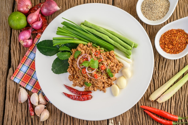 Spicy Minced Pork Salad on a white plate with red onion, lemon grass, garlic, yardlong beans, kaffir lime leaves, and spring onion