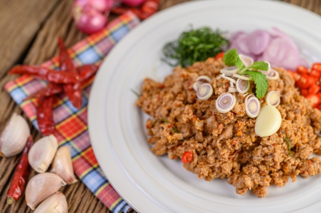 Spicy Minced Pork Salad on a white plate with red onion, lemon grass, garlic, yardlong beans, kaffir lime leaves, and spring onion