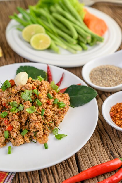 Spicy Minced Pork Salad on a white plate with red onion, lemon grass, garlic, yardlong beans, kaffir lime leaves, and spring onion