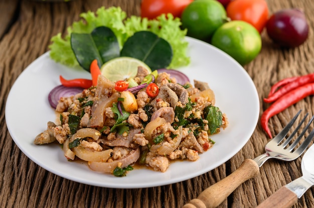 Free photo spicy minced pork salad on a white plate on wooden table.