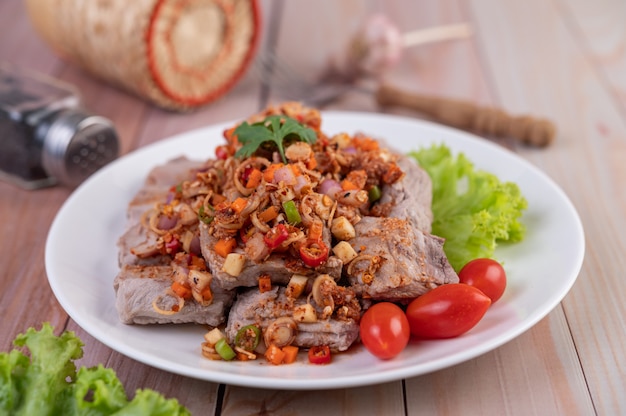 Spicy pork minced with tomatoes and lettuce on a white plate on a wooden table.