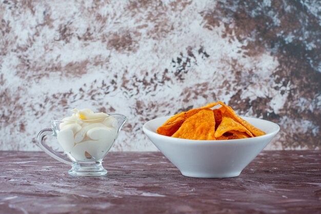 Spicy potato chips in a bowl and yogurt in a glass, on the marble table. 