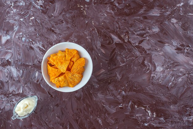 Spicy potato chips in a bowl and yogurt in a glass, on the marble table. 