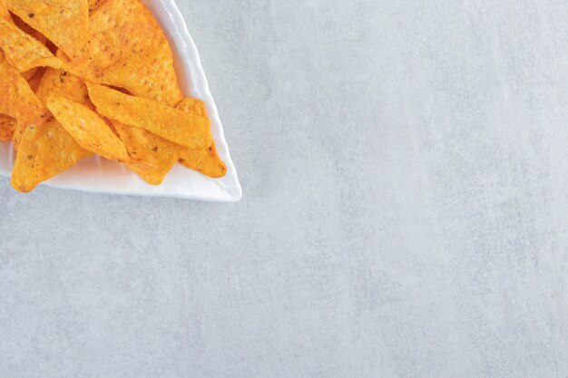 Spicy tortilla chips on leaf-shaped plate on stone