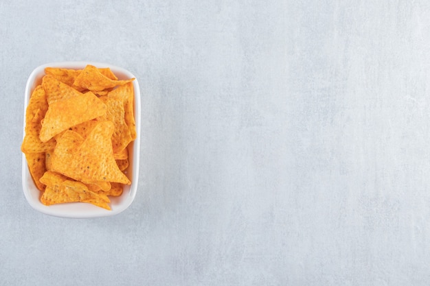 Free photo spicy triangle chips in white bowl on stone.