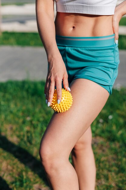 Spiky rubber massage ball in hands of young woman in shorts for cellulite reduction and weight loss ...