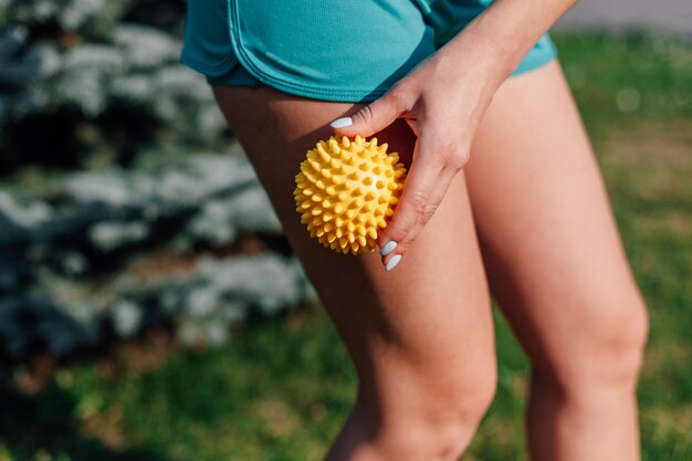 Spiky rubber massage ball in hands of young woman in shorts for cellulite reduction and weight loss ...