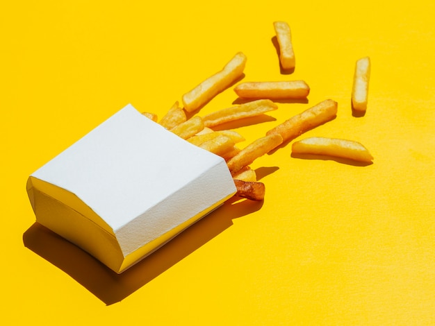 Бесплатное фото Пролитая коробка с картофелем фри на желтом фоне