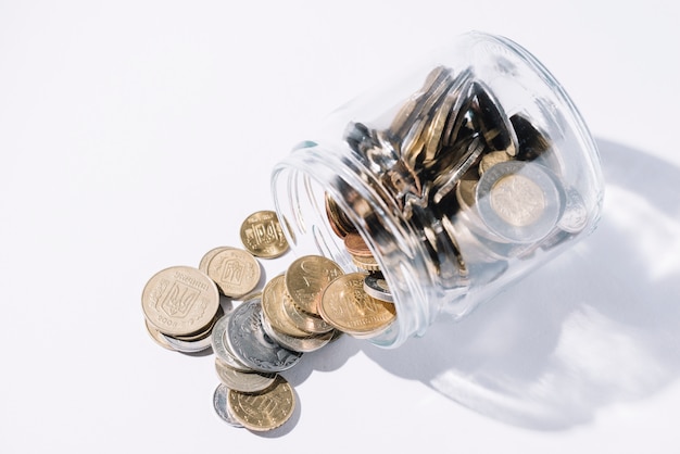 Spilled out coins from glass container on white background