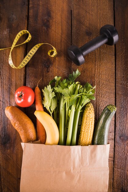 Spilled out vegetables from paper bag near dumbbell and measuring tape