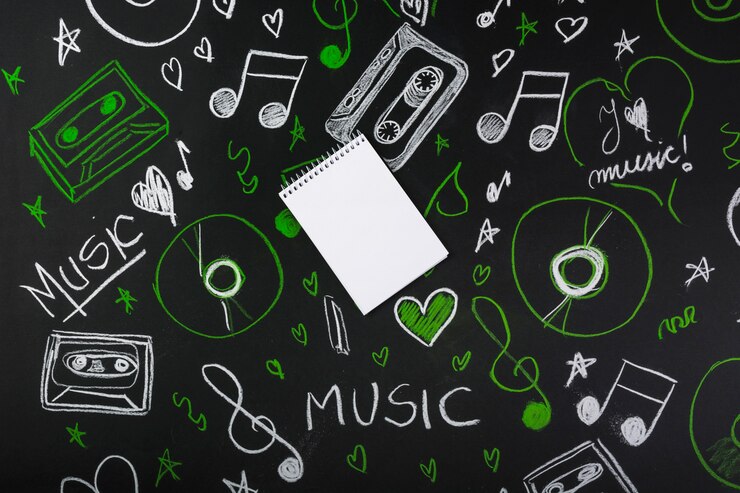 Free Photo spiral blank notepad over the blackboard with drawn musical notes; cassette tapes; compact discs
