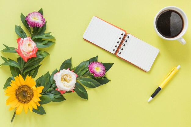 Спиральный блокнот; черный чай; ручка и цветы на цветном фоне