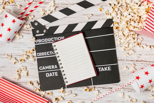 Spiral notepad; clapperboard; drinking straw and popcorns on wooden desk