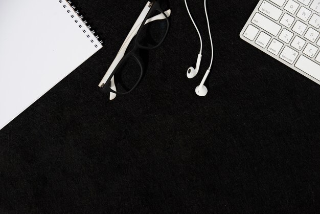 Spiral notepad; eyeglasses; earphone and keyboard on black background