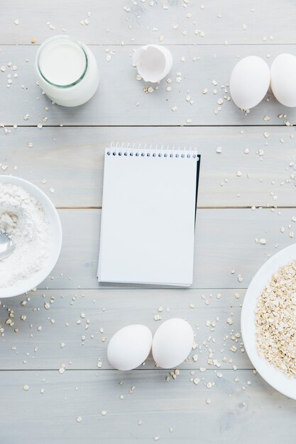 Spiral notepad; oats; eggs; flour and milk on wooden background