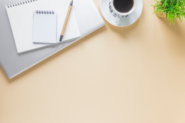 Spiral notepad and pen on laptop with coffee cup on beige background