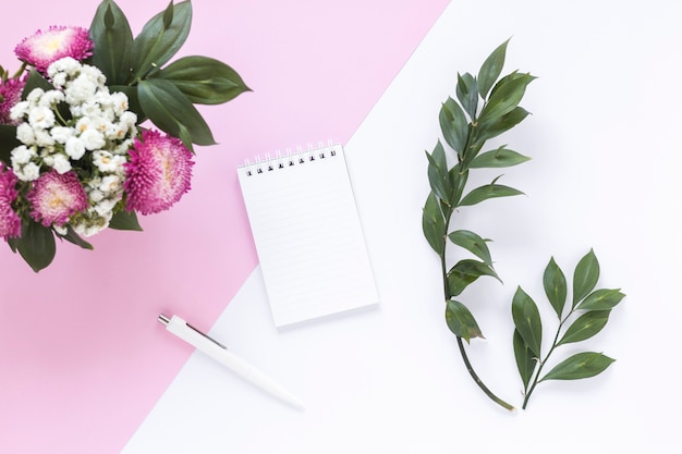 Spiral notepad; pen; leaves and bunch of flowers on dual background