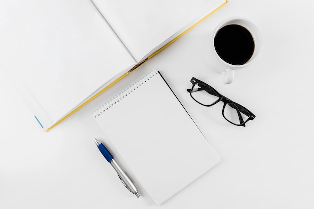 Spiral notepad; spectacles; cup; pen and book on white background