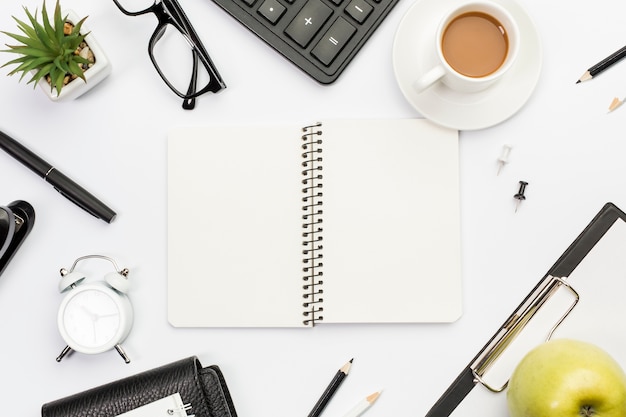 흰색 사무실 책상에 문구, 사과와 커피로 둘러싸인 나선형 메모장