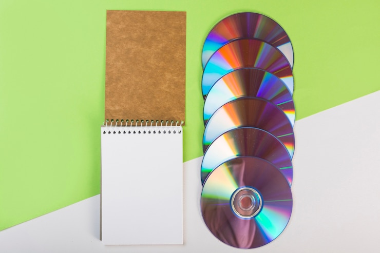 Free Photo spiral notepad with colorful compact discs on green and white dual background