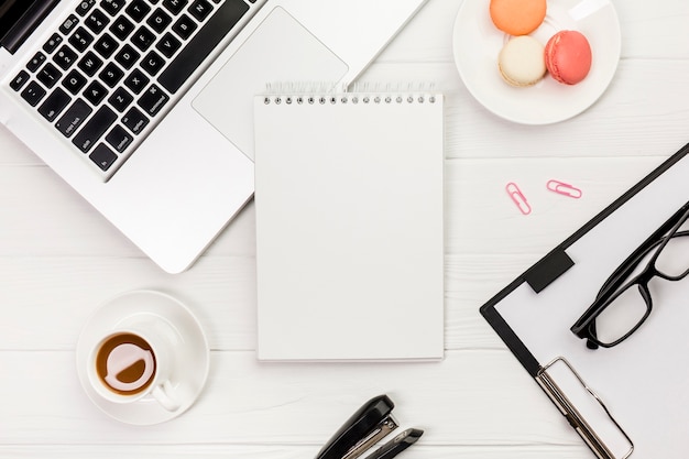 노트북, 마카롱, 클립 보드와 흰색 사무실 책상에 안경 커피 컵과 나선형 메모장