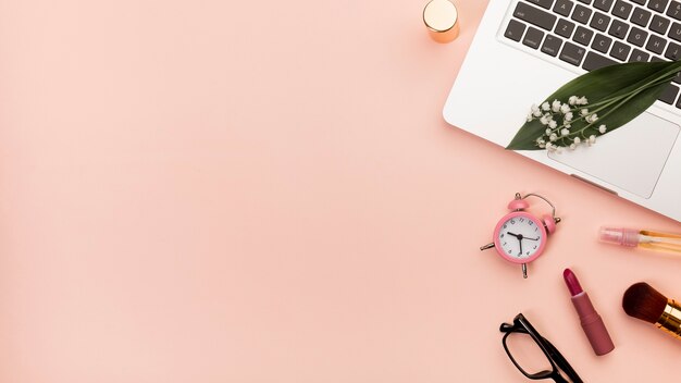 Spiral notepad with lipstick,alarm clock,eyeglasses on laptop against peach backdrop