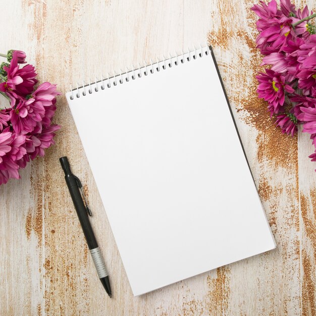 Spiral notepad with pen and pink flowers on wooden textured background