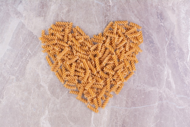 Spiral shape pastas in heart shape on the marble. 