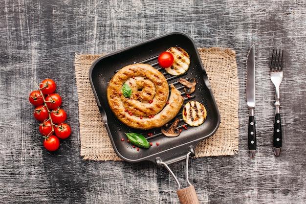 Спираль вкусные жареные колбаски в кастрюле с овощами на текстурированном фоне