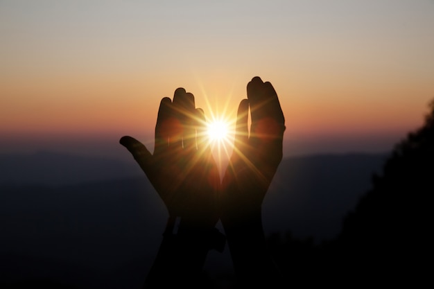 太陽の上の精神的な祈りの手がぼやけて美しい夕日と輝き