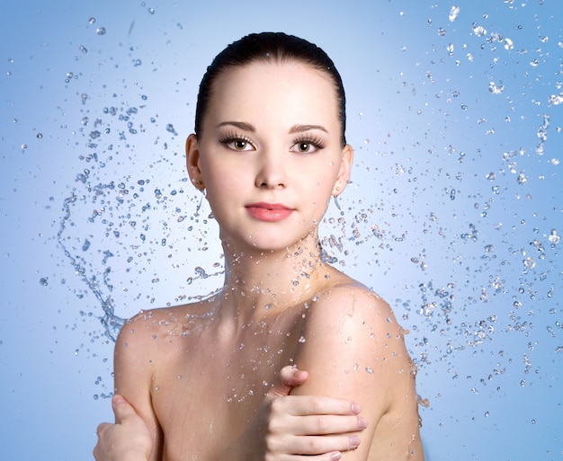 Бесплатное фото Брызги воды на красивой молодой женщине с чистой свежей кожей - цветной фон