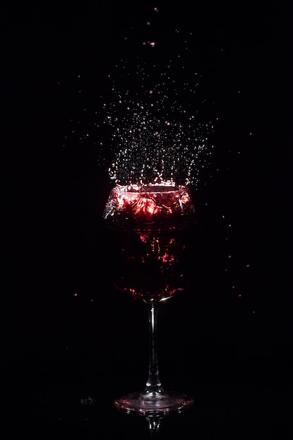 Splashes of red juice fly around crystal wineglass standing in dark space