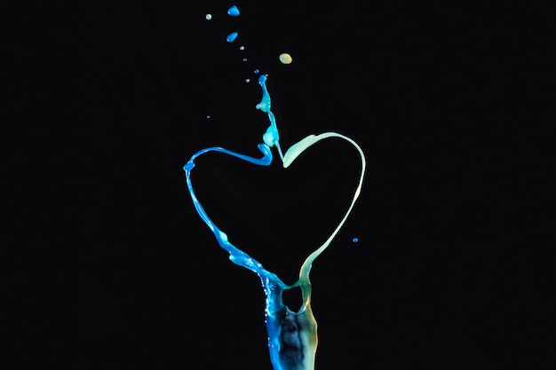 Splashing colorful liquid forming heart shape over dark backdrop