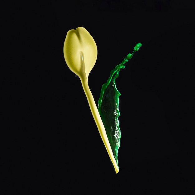 Splashing yellow and green paint forming flower bud over dark backdrop
