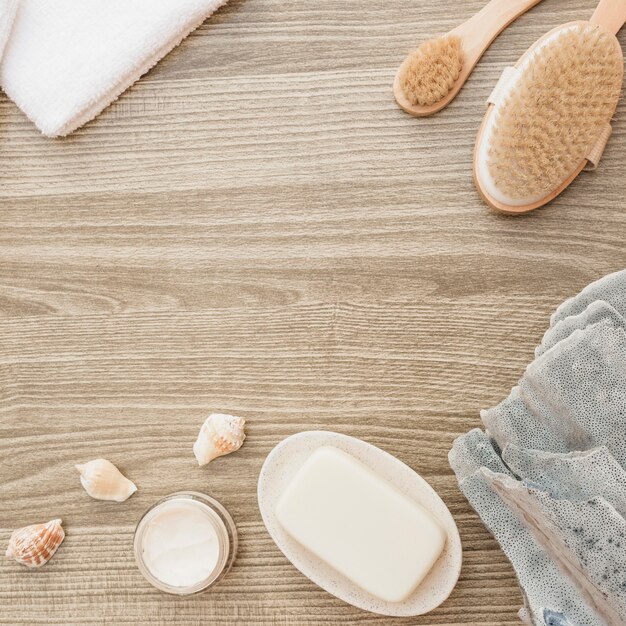 Sponge; seashell; soap; brush; towel and moisturizing cream on wooden surface