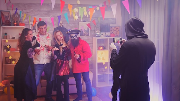 Spooky characters taking a group photo at halloween party in decorated room.