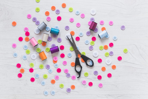 Free photo spool and scissor on spread colorful buttons over white textured background