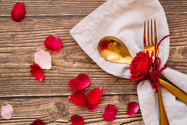 Foto gratuita cucchiaio e forchetta con fiore rosso sul tovagliolo vicino a petali