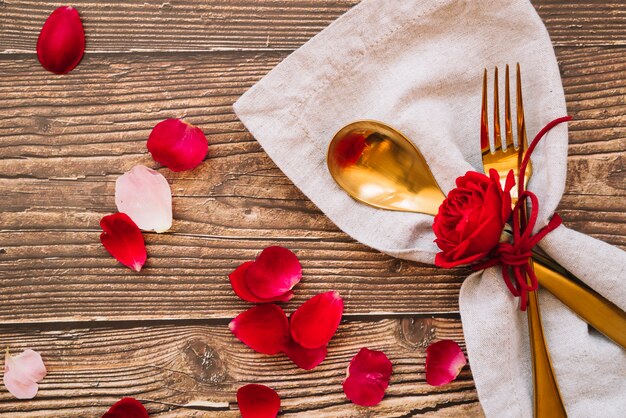 Spoon and fork with red flower on napkin near petals