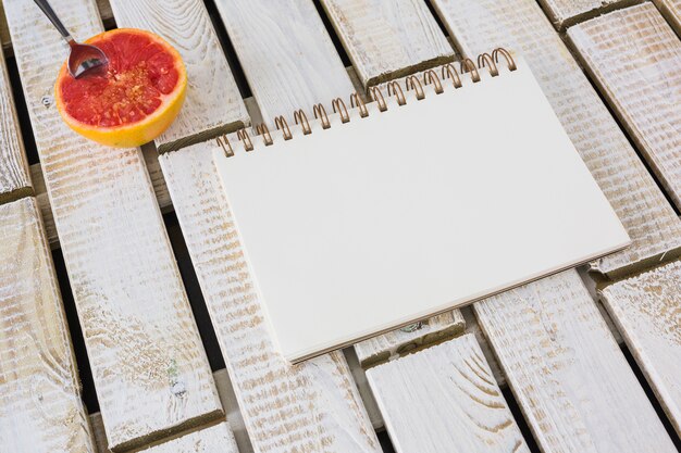 Spoon in the halved grapefruit with spiral notebook on pattern background