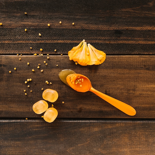 Spoon of honey near flower petals and candies on wooden background