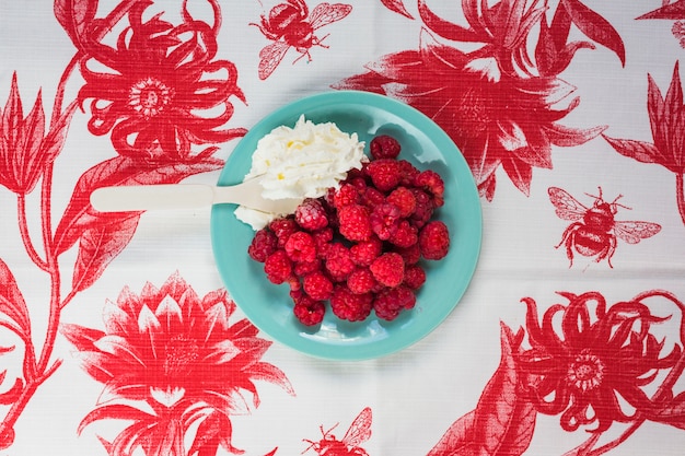 Spoon in whipped cream with raspberries on blue plate over the floral table cloth