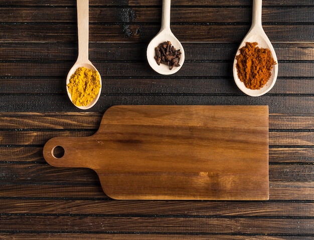 Spoons with spices near cutting board