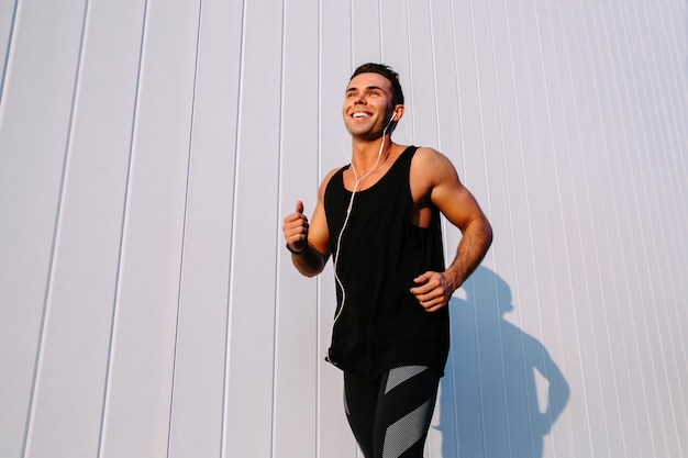 Sport concept. Smiling handsome muscular guy running outdoors, against the white wall