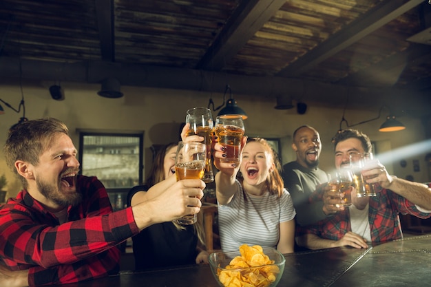 Sport fans cheering at bar, pub and drinking beer while championship, competition is going