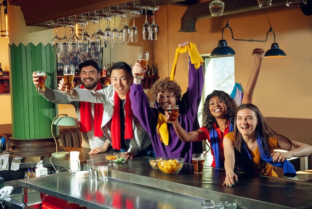 Sport fans cheering at bar, pub and drinking beer while watching a sport competition.