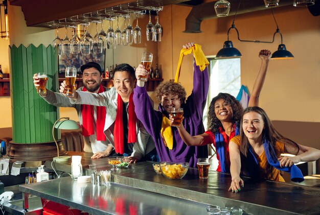 Sport fans cheering at bar, pub and drinking beer while watching a sport competition.