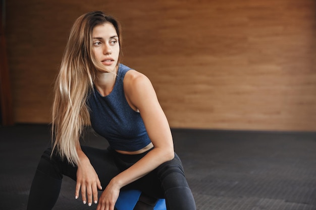 Free photo sport fitness and endurance concept gorgeous young fitness insctructor sportswoman in activewear with long blond hair sit medicine ball near wooden gym wall turn aside rest before workout