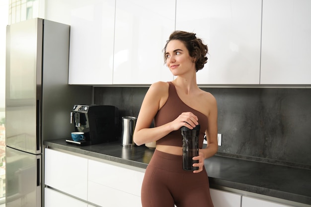 Sport and healthy lifestyle portrait of smiling fitness woman in activewear standing near kitchen co