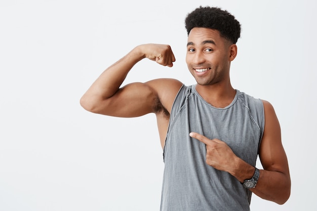 Sport and lifestyle concept. Dark skinned handsome man with curly hair showing muscles. Professional sportsmen posing for article about spot career with happy expression